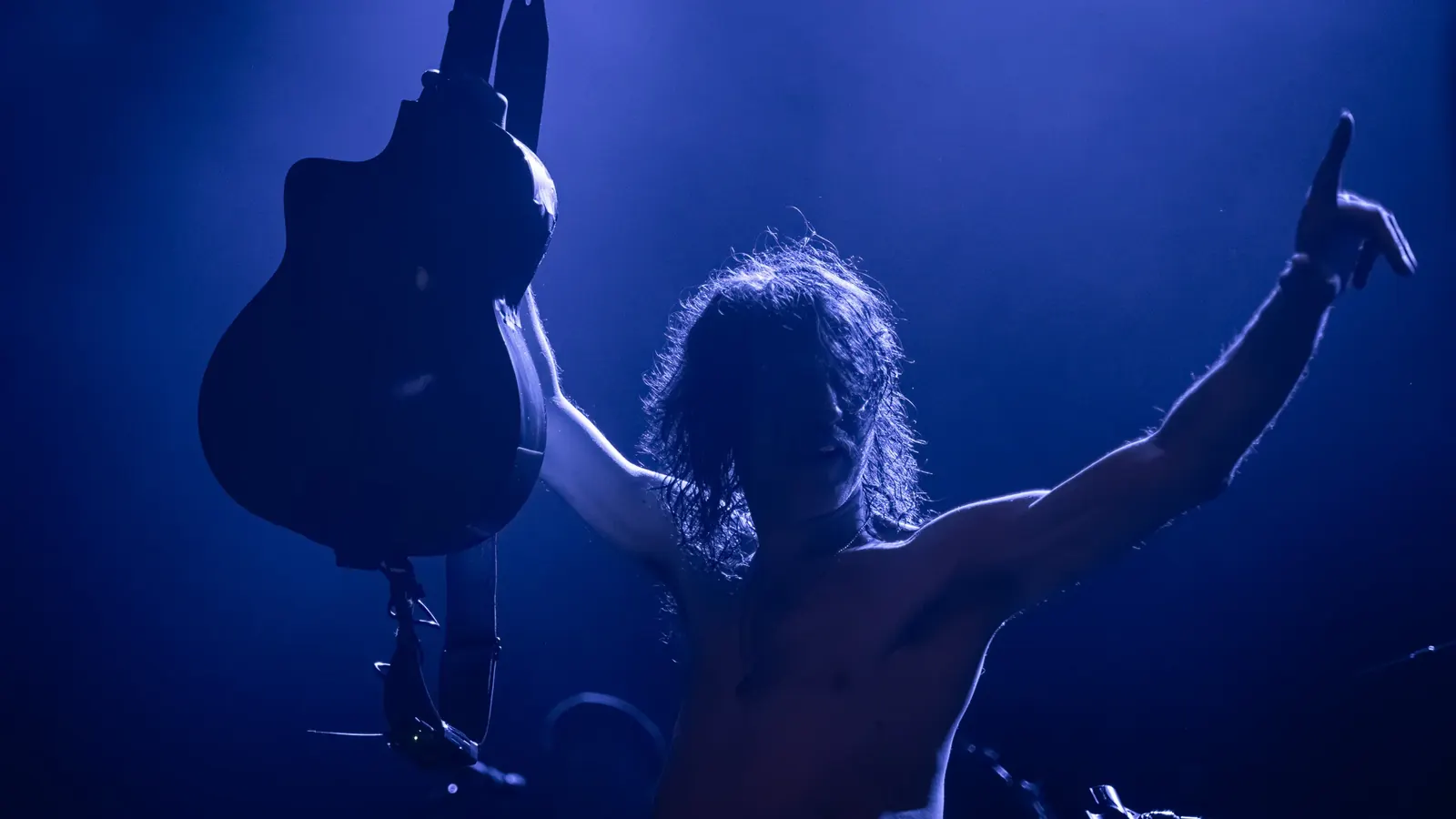 Musician raising a guitar under blue lights